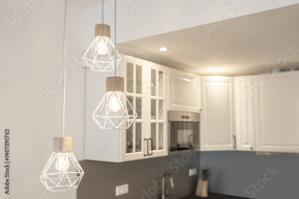 Fototapeta Stylish modern kitchen with geometric pendant lights and white cabinetry. Soft lighting creates a cozy and elegant interior design.