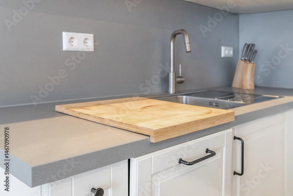 Fototapeta Modern kitchen countertop with a wooden cutting board, stainless steel sink, faucet, and knife block. Minimalist and clean kitchen design in neutral tones.
