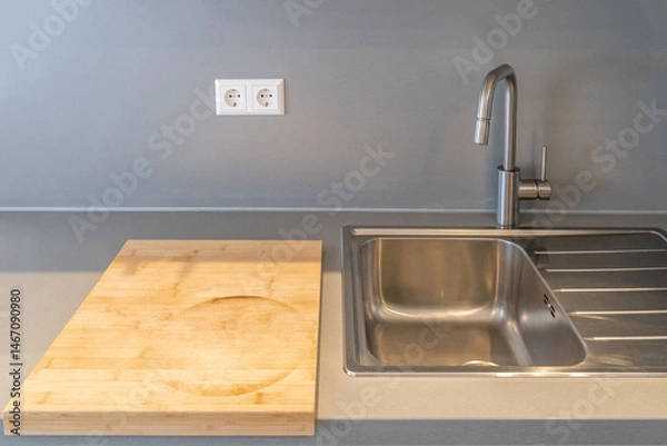 Fototapeta Modern kitchen countertop with a wooden cutting board, stainless steel sink, faucet, and knife block. Minimalist and clean kitchen design in neutral tones.