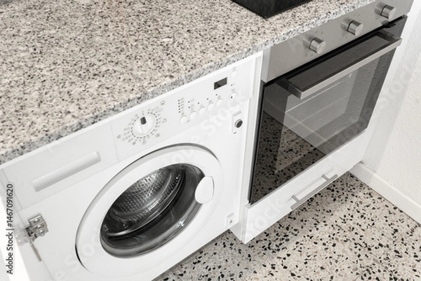 Fototapeta Close-up view of a modern kitchen interior featuring a built-in washing machine and an electric oven under a granite countertop.