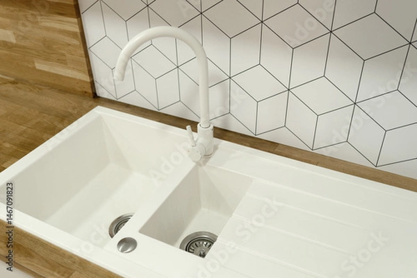 Fototapeta Modern white kitchen sink with double basins and curved faucet. Geometric tile backsplash and wooden countertop create a stylish, minimalist kitchen design.