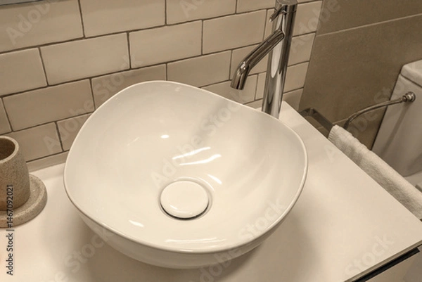 Fototapeta Modern bathroom sink with an irregularly shaped ceramic bowl and a tall chrome faucet. Stylish interior featuring subway tile backsplash and minimalist design.