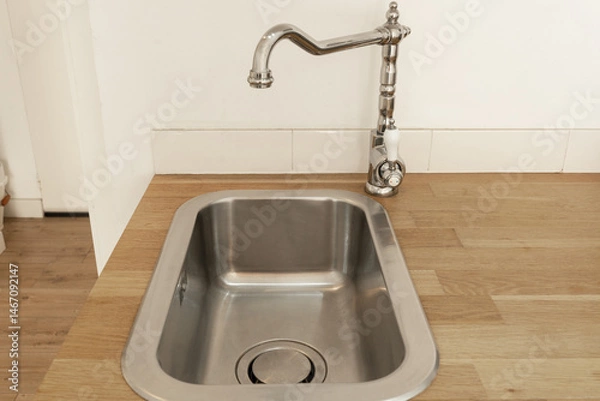 Fototapeta Modern stainless steel kitchen sink with a vintage-style chrome faucet, set in a wooden countertop. Minimalist interior design with clean lines and natural materials, creating a bright and functional