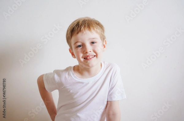Obraz boy 5 years old with blond hair and blue eyes in a white t-shirt on a white background smiling and posing for the camera