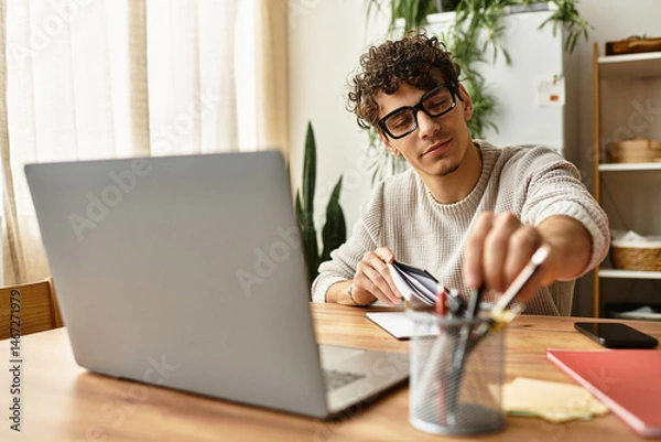 Fototapeta Stylish young man organizing desk tools while working in a cozy home office during the day