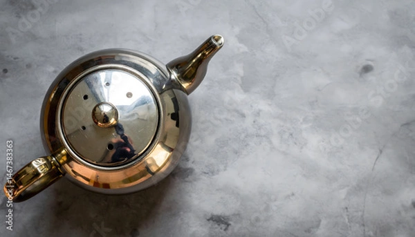 Fototapeta a close up photograph of a gold tea kettle with a visible spout placed on a marble surface against a blurred background