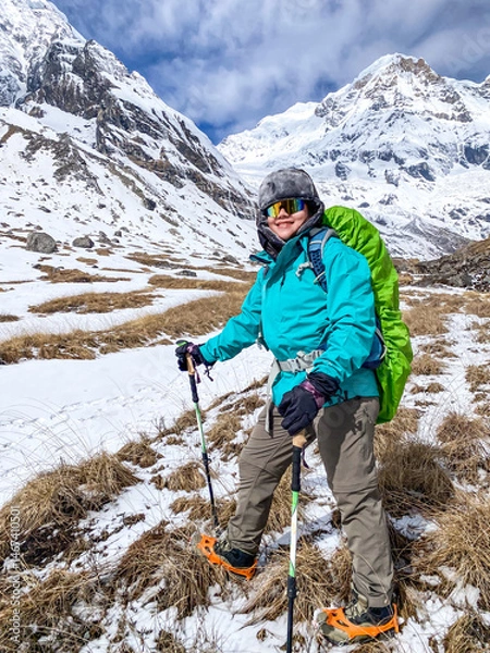 Obraz Young asian female hiker took photos after successfully hiking to Annapurna Base Camp, with the snow-capped Himalayan peaks visible in the morning