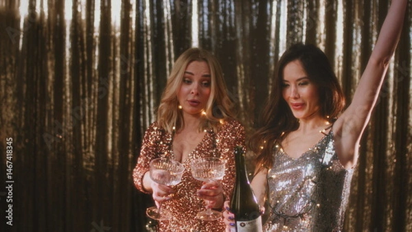 Fototapeta The girl opens a bottle of champagne. A woman in a sparkling dress uncorks a bottle of alcohol