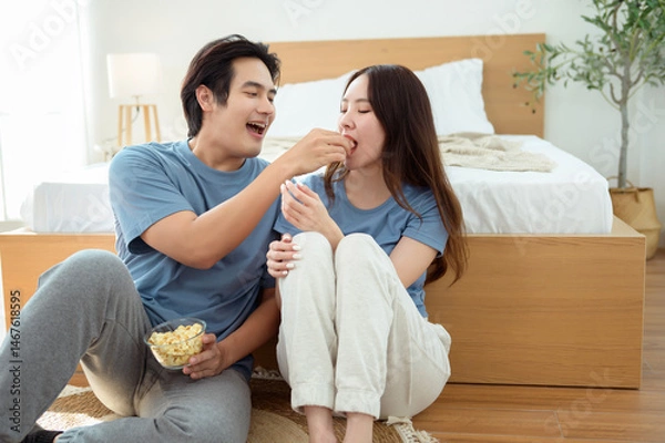 Fototapeta Couple Enjoying Popcorn Together While Sitting on the Floor in a Cozy Bedroom During the Afternoon
