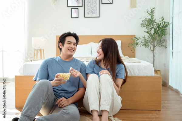 Fototapeta Couple Enjoying Popcorn Together While Sitting on the Floor in a Cozy Bedroom During the Afternoon