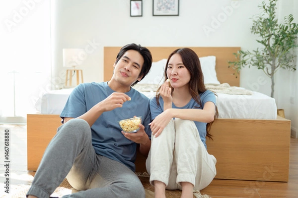 Fototapeta Couple Enjoying Popcorn Together While Sitting on the Floor in a Cozy Bedroom During the Afternoon