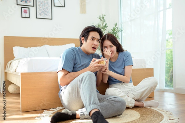 Fototapeta Couple Enjoying Popcorn Together While Sitting on the Floor in a Cozy Bedroom During the Afternoon