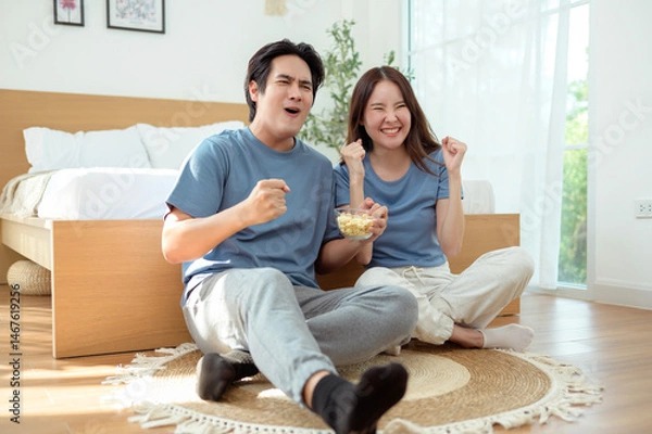 Fototapeta Couple Enjoying Popcorn Together While Sitting on the Floor in a Cozy Bedroom During the Afternoon