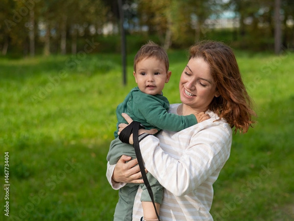 Fototapeta Caucasian woman holds her one-year-old son in her arms while walking in the park in autumn. 
