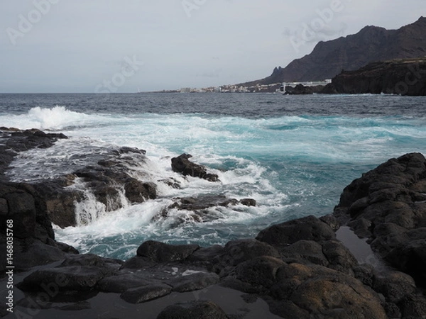 Fototapeta Volcanic coast of Tenerife island: blue water of Atlantic ocean, black rocky shore and lava rocks on the horizon. Holidays in Canary Islands, Spain.