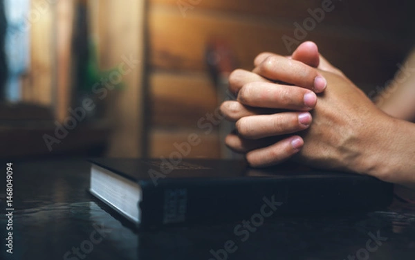 Fototapeta Close up of a man praying, hands clasped together on Bible, devotional concept.