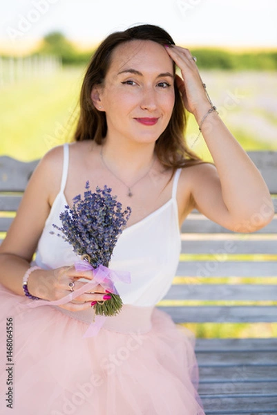 Obraz a beautiful girl in a dress with a bouquet of lavender flowers sits on a bench
