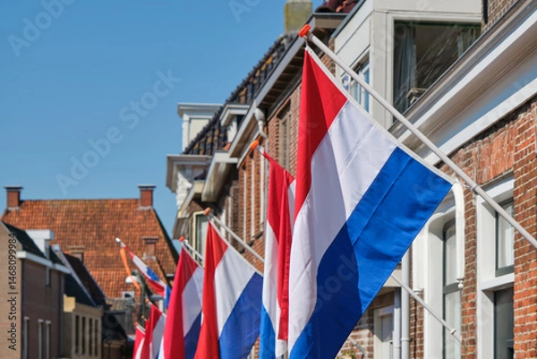 Fototapeta Dutch flags in a typical dutch street on Koningsdag under a blue sky. Koningsdag is a national holiday in the Kingdom of the Netherlands.	