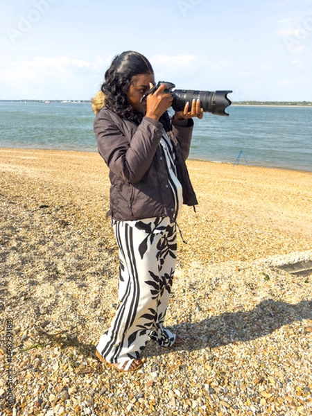 Obraz Calshot Hampshire England UK. 27.04.2025. African woman using an DSLR digital camera while on a visit to Calshot beach in Hampshire UK