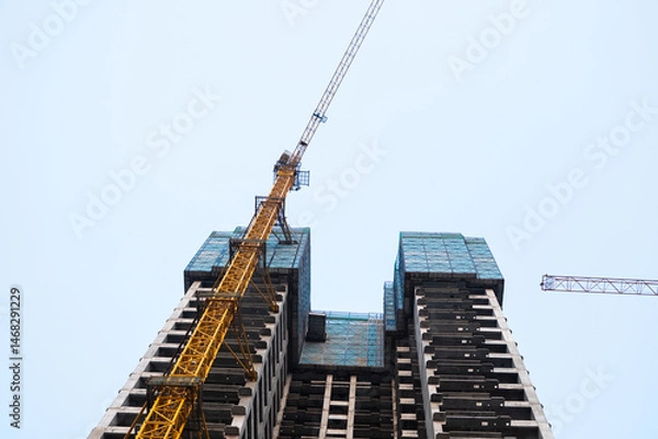 Fototapeta Low-angle view of skyscraper and tower crane under construction
