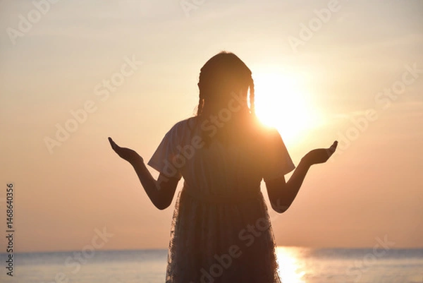 Fototapeta little girl closed her eyes, praying on a sea during beautiful sunset. Hands folded in prayer concept for faith, spirituality and religion. Peace, hope, dreams concept