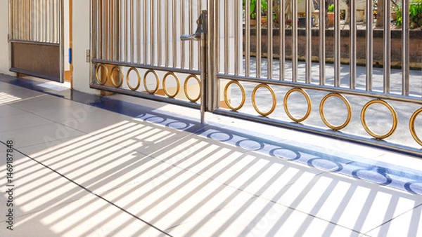 Fototapeta Silver and golden stainless steel gate door with light and shadow on white tile floor in patio area of vintage house, Exterior architecture background in perspective side view