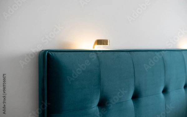 Obraz Elegant Teal Velvet Headboard Against A White Wall Illuminated By A Warm Toned Brass Wall Sconce Creating A Sophisticated Atmosphere
