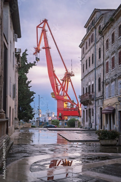 Fototapeta Harbour view of a red crane towering above wet streets in Pula, Croatia during the early evening