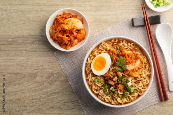 Fototapeta Instant noodle soup with kimchi and boiled egg in white bowl on wood table.Korean style.Top view with copy space.