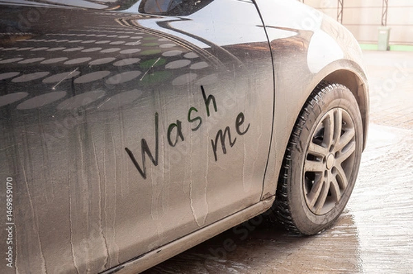 Fototapeta Close-up of a dirty car door with a handwritten "Wash me" message requesting a clean.