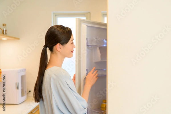 Obraz 冷蔵庫の中身を真剣に見つめる女性が朝の支度をしている静かなキッチン風景