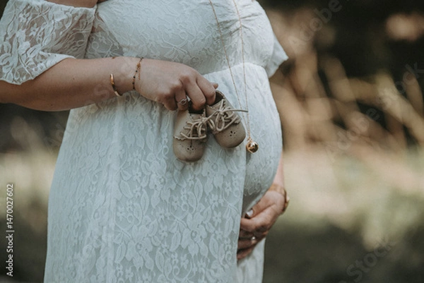 Fototapeta Une femme enceinte avec des petits chaussons de bébé sur son ventre