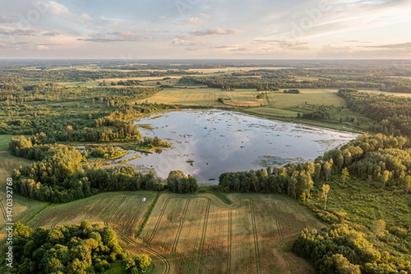Fototapeta Vast landscape with tranquil lake surrounded by lush greenery and farmland at sunset