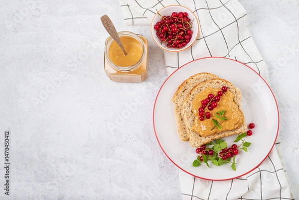 Fototapeta Whole grain sandwich with peanut butter and red currant berries top view on light background with copy space