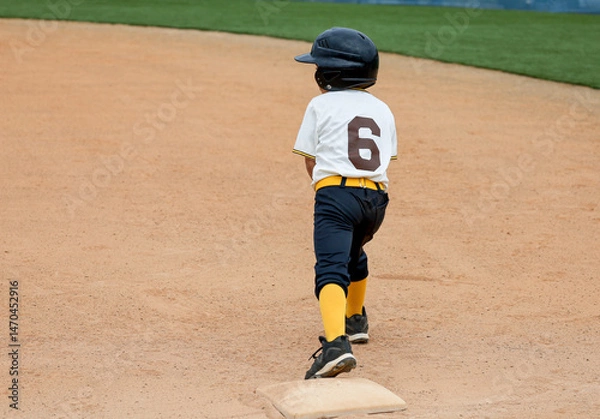 Obraz A six year old baseball player boy on first base ready to run.