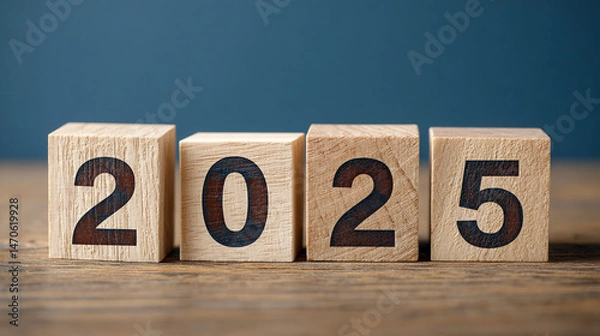 Fototapeta Wooden blocks displaying 2025 on a wood surface against a blue background, symbolizing the upcoming year and new beginnings