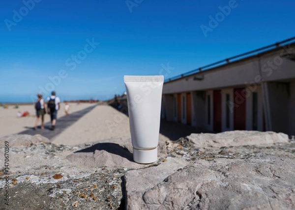 Obraz body lotion stands upright on a stone wall at the beach with a sandy walkway and seaside buildings in the background under a clear sky