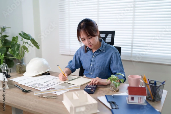 Fototapeta Asian Women Architect Working on Blueprints for House Design Planning and Calculating Building Cost for Construction Planning her dream home Building Projects