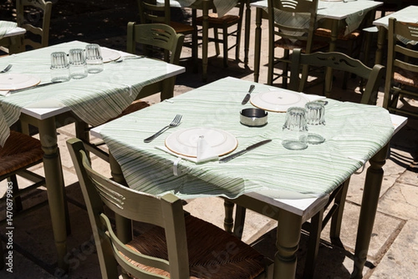 Fototapeta Outdoor Taverna Table Setting. Traditional Greek taverna table set with plates and glassware, shaded and ready for guests in Zakynthos, Greece.