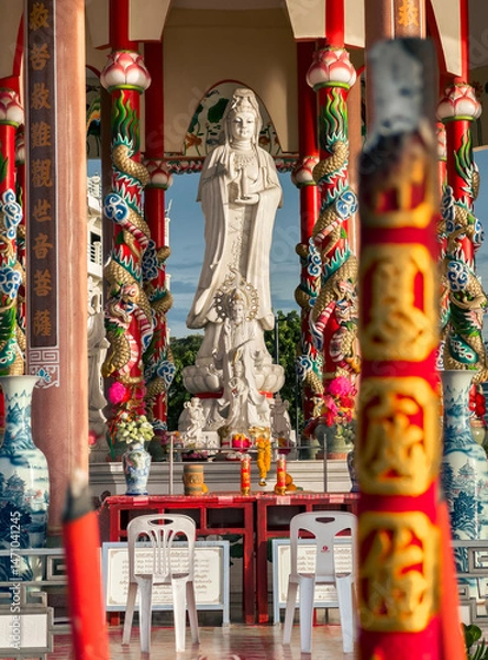 Fototapeta Large statue of Guanyin in colorful temple with dragon columns during sunny afternoon. Sriracha, Thailand.