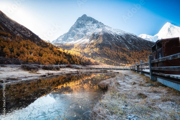 Obraz Snow capped mountain, autumn forest, wooden fence, and calm reflective water create peaceful landscape with clear blue sky and golden trees, evoking tranquility and natural beauty