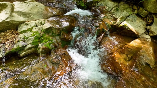 Fototapeta Slow Motion Drone Footage of Crystal-Clear Stream Flow in a Serene Forest Valley, Featuring Gentle Ripples, Tranquil Water Sounds, and the Pristine Beauty of Nature