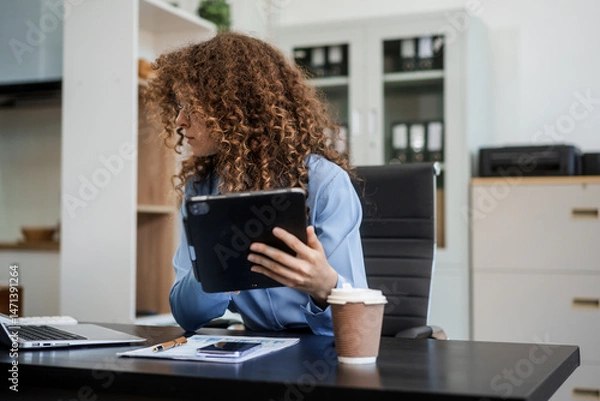 Obraz Confident Russian businesswoman sits indoors at her desk, dressed in formal attire,  paperwork and planning. Stylish and efficient, she manages tasks, notes ideas, and leads with professionalism.