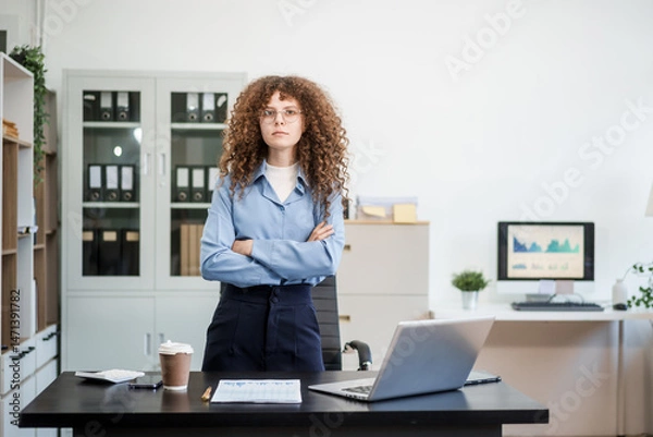 Obraz Confident Russian businesswoman sits indoors at her desk, dressed in formal attire,  paperwork and planning. Stylish and efficient, she manages tasks, notes ideas, and leads with professionalism.