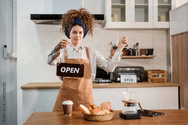 Obraz A young woman with curly hair and a headband, wearing a brown apron, prepares pour-over coffee on a wooden countertop in a bright kitchen. Focused and calm, she enjoys her morning routine.