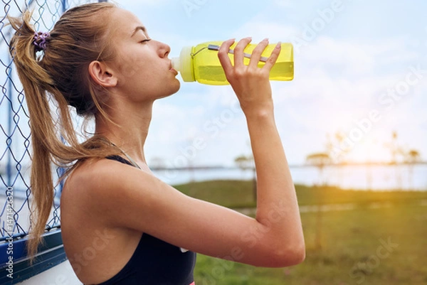 Fototapeta Woman drinking water at workout outdoors
