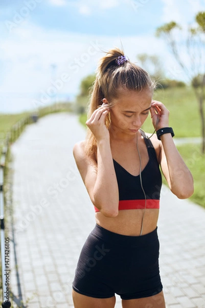 Fototapeta Young fit woman wearing earphone for work out outdoor