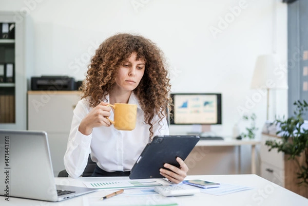 Obraz Confident Russian consultant sits at modern desk, analyzing market data on laptop. reports and charts, she embodies precision, leadership, and strategic mindset of corporate consulting.