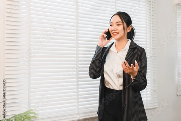 Fototapeta Businesswoman office communication phone conversation professional smiling standing window blinds emotionally expressing confidence while talking on mobile phone in modern office setting