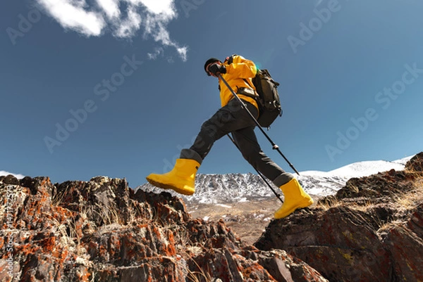 Obraz Bottom view of male trekker stepping from rock to rock in mountains on sunny day, low angle view